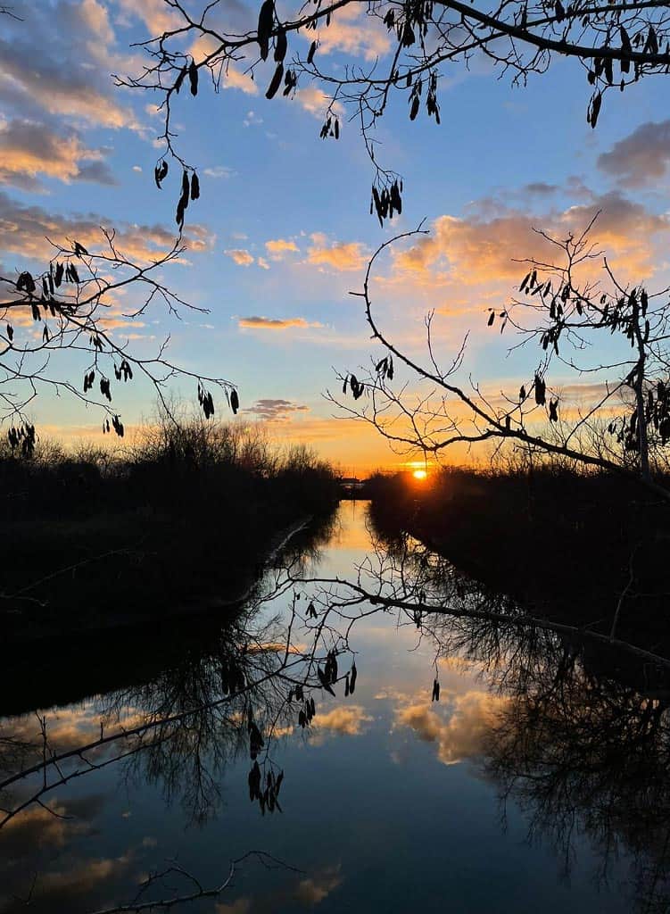 Tramonto sui canali della laguna con sole e nuvole che si specchiano in acqua
